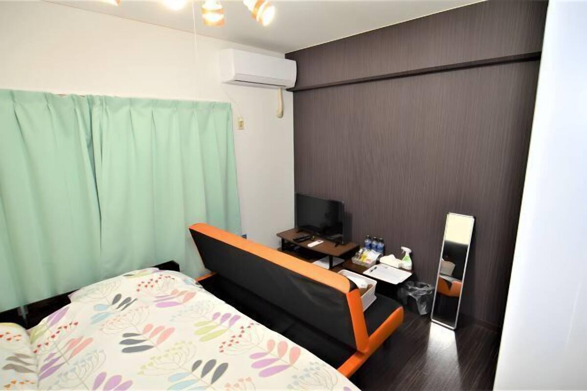 A hotel room with a bed, a desk with a computer, a mirror, and a TV.