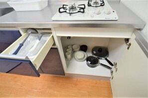 A kitchen with a gas stove, a drawer with utensils, and a cabinet with dishes. - Comfort CUBE PHOENIX Miyazaki (Miyazaki)