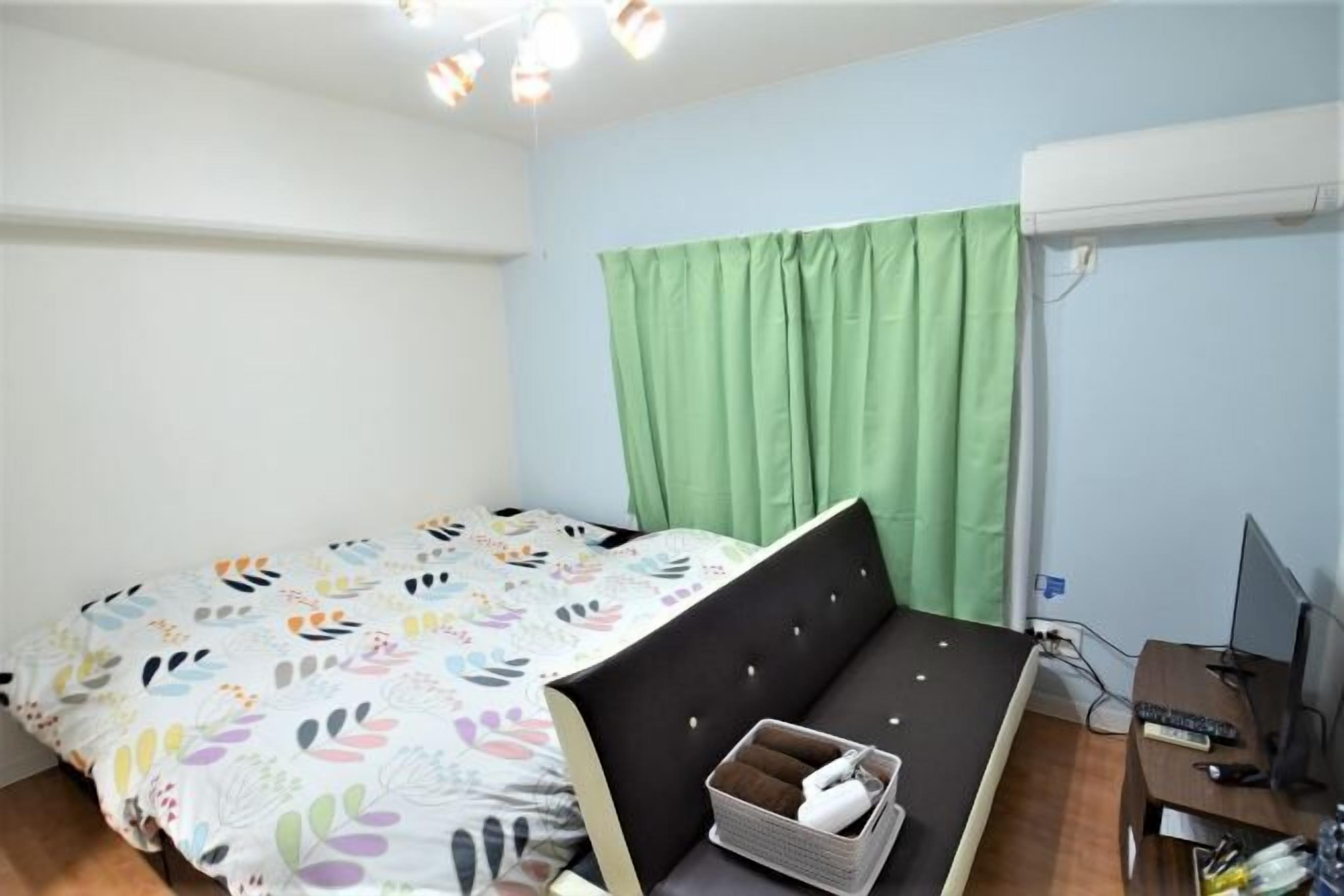Un dormitorio con una cama, un escritorio, una computadora y una cortina verde.