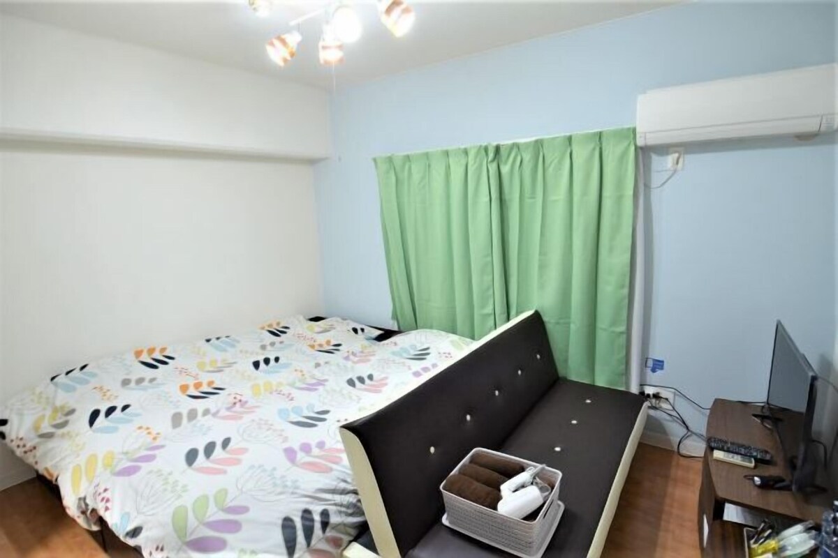 A bedroom with a bed, a desk, a computer, and a green curtain.