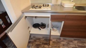 Una cocina compacta con estufa a gas, un estante con utensilios de cocina y un lavamanos.