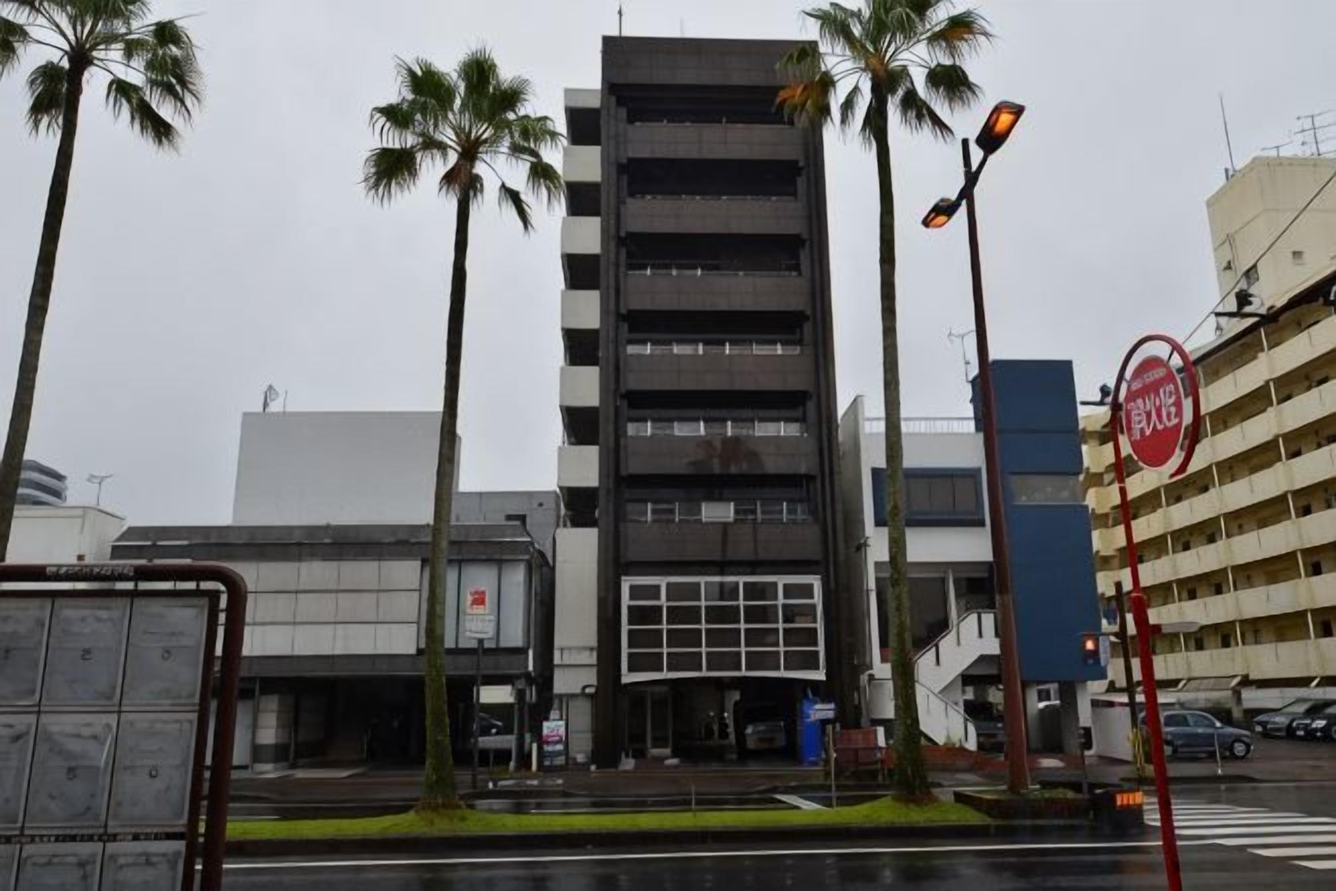 A multi-story building with a modern design, a parking garage, and palm trees.