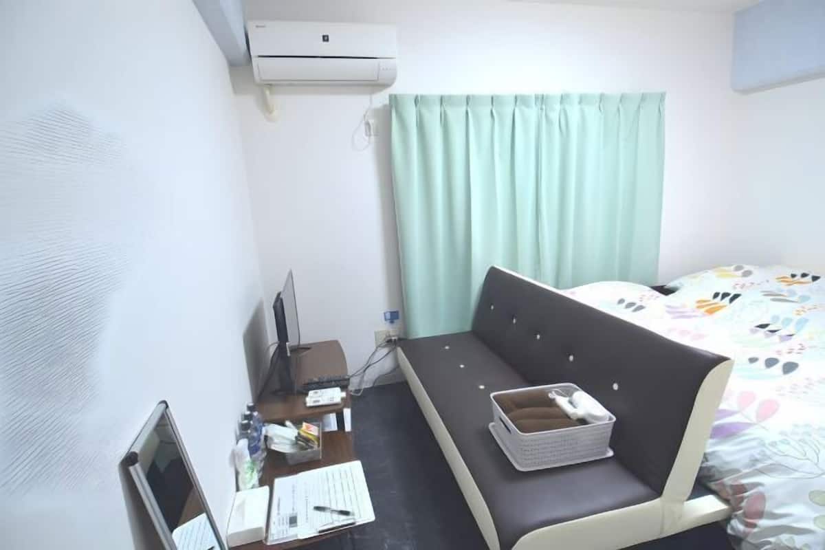 A hotel room with a bed, a desk with a laptop, a chair, a small table, and a window with curtains.