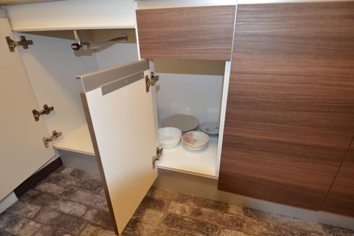 A bathroom with a white sink, a wooden cabinet, and a shelf with plates and bowls.