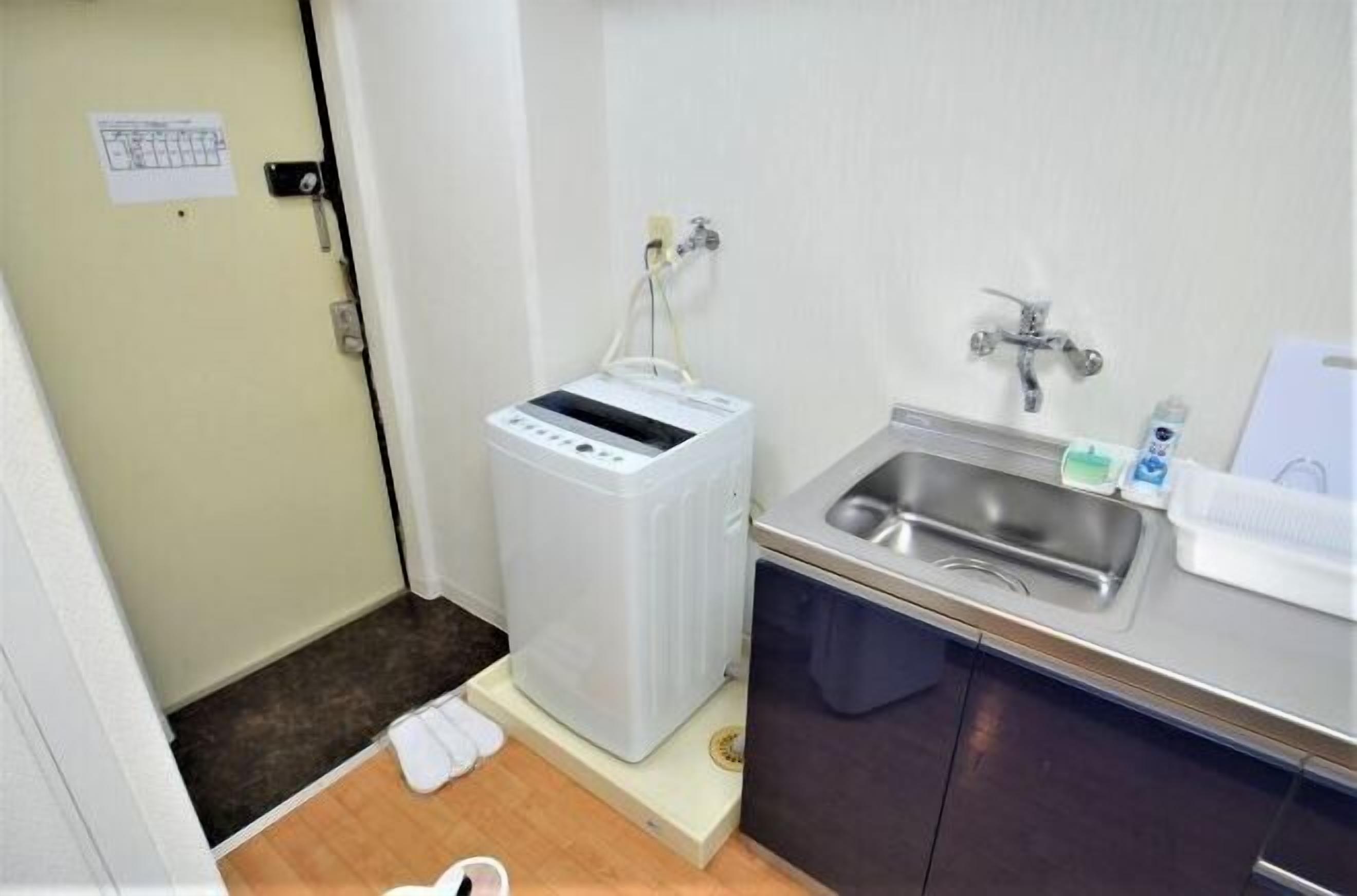 Une chambre d’hôtel compacte équipée d’une machine à laver, d’un lavabo et d’un petit plan de travail avec des articles de toilette.