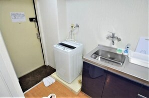 Une chambre d’hôtel compacte équipée d’une machine à laver, d’un lavabo et d’un petit plan de travail avec des articles de toilette.