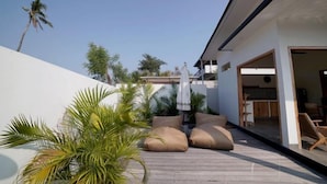 A modern outdoor patio with a wooden deck, beige cushions, and a white umbrella. - 1BR Villa with Private Pool in Amed (Bali)