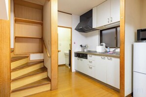 A kitchen with white cabinets, a black range hood, and a microwave. - Asakusa old town guesthouse (Tokyo)