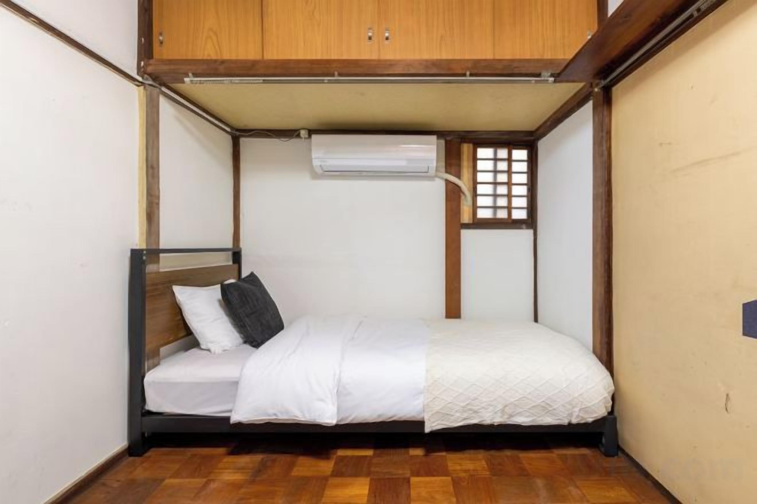 Een kleine, compacte kamer met een enkel bed, een houten garderobe en een raam met een ruitpatroon.