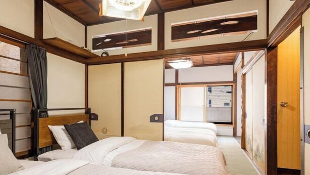 A traditional Japanese-style room with two beds, wooden beams, tatami flooring, and sliding doors.