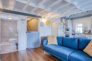 A modern interior with a blue sofa, a kitchen area, and a bathroom. - Beachwood - 2 Bedroom Cottage - Penally (Tenby)