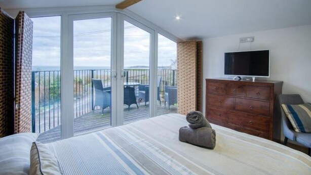 A bedroom with a bed, a television, a dresser, and a balcony with outdoor furniture.