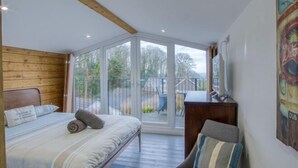 A bedroom with a bed, a chair, a desk, and a large glass door leading to an outdoor area.