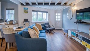 A modern living room with a sofa, a television, a dining area with a table and chairs, and a kitchen area.