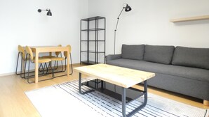A modern living room with a wooden dining table, a grey sofa, and a black bookshelf. - RentPlanet - Apartament Brneńska (Poznań)