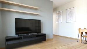 A modern living room with a flat-screen TV, wooden shelves, a dining table with chairs, and two framed artworks on the wall. - RentPlanet - Apartament Brneńska (Poznań)