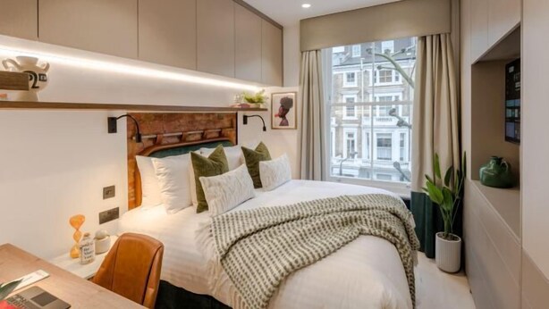 A modern hotel room with a large bed, a desk, and a window with a city view. - Kensington King Studio G (London)