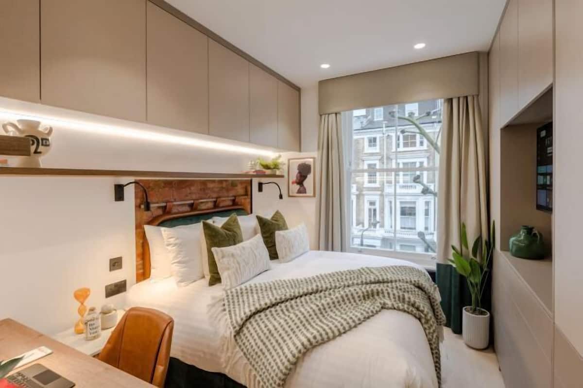 A modern hotel room with a large bed, a desk, and a window with a city view.