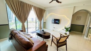 A modern living room with a sofa, a dining table, a TV mounted on the wall, and a ceiling fan. - NEW Serenity@Teega ResidenceL2 by UcomeHomestay (Iskandar Puteri)