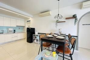 A modern kitchen with white cabinets, a black refrigerator, and a dining area with a table set for four. - NEW Serenity@Teega ResidenceL2 by UcomeHomestay (Iskandar Puteri)
