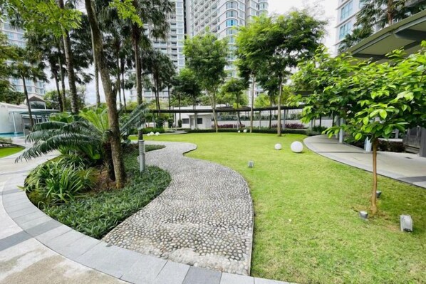 A landscaped courtyard with a curved pathway, trees, and a grassy area. - NEW Serenity@Teega ResidenceL2 by UcomeHomestay (Iskandar Puteri)
