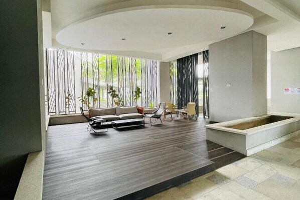 A modern living room with a sofa, chairs, and a small table. There is a window with vertical blinds and a view of greenery outside. - NEW Serenity@Teega ResidenceL2 by UcomeHomestay (Iskandar Puteri)