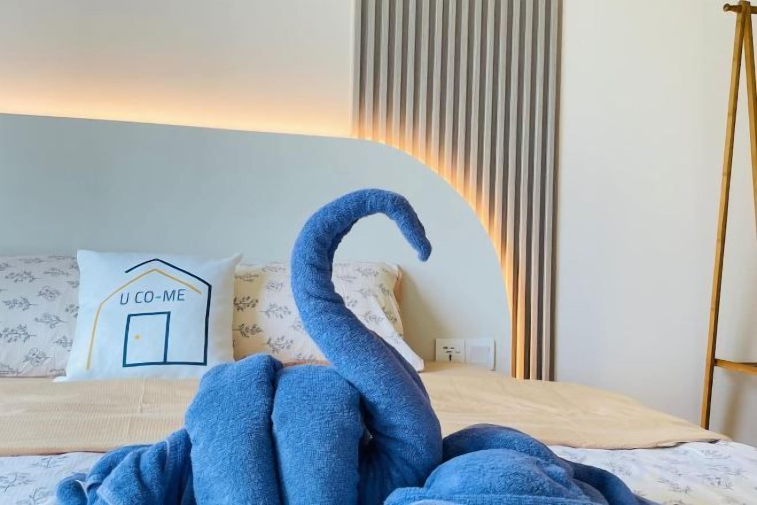 A bed with a swan-shaped pillow and a pillow with 'U CO-ME' text.