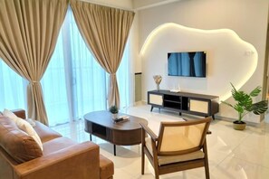 A modern living room with a sofa, a coffee table, a TV, and a plant. - NEW Serenity@Teega ResidenceL2 by UcomeHomestay (Iskandar Puteri)