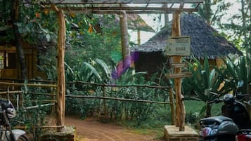 A rustic wooden gate leading to a thatched-roof structure, a signpost with directions, and a motorcycle parked nearby.