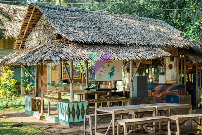 A rustic hut with a thatched roof, wooden benches, and a colorful mural.