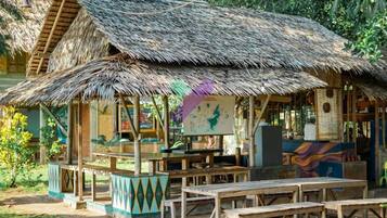 A rustic hut with a thatched roof, wooden benches, and a colorful mural.
