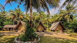 A tropical resort with thatched-roof huts, surrounded by palm trees and a well-maintained lawn. - Bunga Jabe (Karimunjawa)