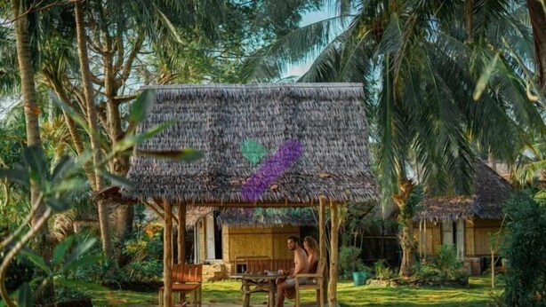 A thatched-roof hut with a wooden bench and table, surrounded by lush greenery and palm trees. - Bunga Jabe (Karimunjawa)