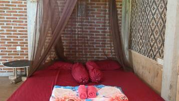 A single bed with a red bedspread, a floral blanket, and a mosquito net.