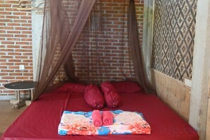 A single bed with a red bedspread, a floral blanket, and a mosquito net. - Bunga Jabe (Karimunjawa)