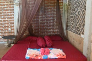 Una cama individual con una colcha roja, un edredón floral y una mosquitera.