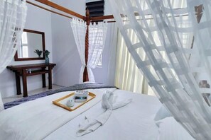 A neatly made bed with a tray of toiletries, a bedside table with a mirror and a small plant, and sheer curtains. - Apartment Casa Klebang Fully Aircon Blissful Suite (Chemor)