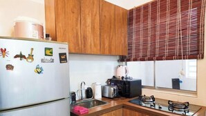 Una cocina compacta con armarios de madera, un refrigerador, un tostador, una tetera y una estufa a gas.