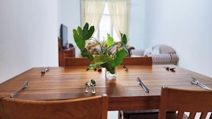 Una mesa de comedor con sillas, una planta y un televisor al fondo.