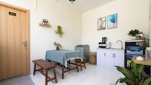 A small, clean room with a wooden door labeled "301", a table with a blue tablecloth, a bench, a small shelf with bottles, a plant, a kettle, a microwave, and a cabinet. - Galaxy Bui vien Street Home (Ho Chi Minh City)