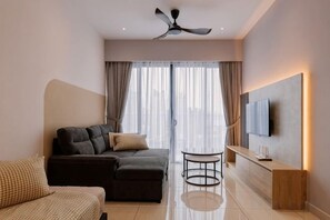 A modern hotel room with a sectional sofa, a small round table, a flat-screen TV mounted on the wall, and a ceiling fan.