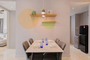 A dining area with a table set for six, chairs, a hanging light fixture, and a refrigerator in the background.