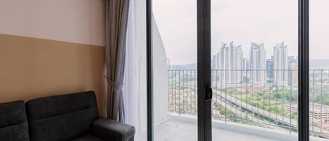 A modern living room with a sofa, a large sliding glass door leading to a balcony with a city view.