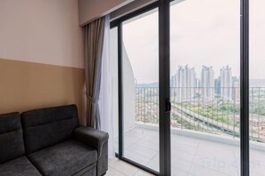 Un salon moderne avec un canapé et une grande porte-fenêtre coulissante donnant sur un balcon offrant une vue sur la ville.