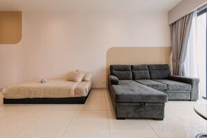 Un salon moderne avec un lit, un canapé d’angle gris et une petite table.