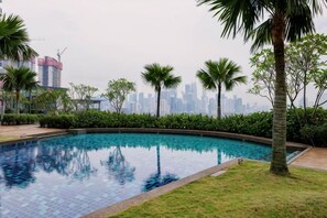 A swimming pool with a city skyline in the background, surrounded by greenery.