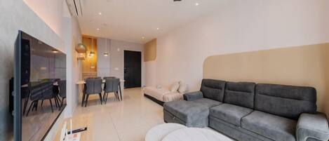 A modern living room with a sectional sofa, a flat-screen TV, a dining area with chairs, and a ceiling fan.