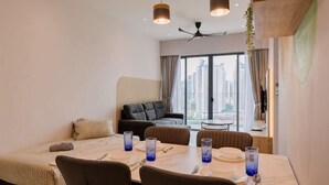 A modern hotel room with a dining area, a sofa, and a large window with a city view. - Datum Jelatek Residence by FEEL HOME (Ampang)