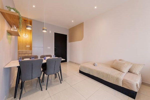 A modern living space with a dining area, a sofa, and a kitchen.