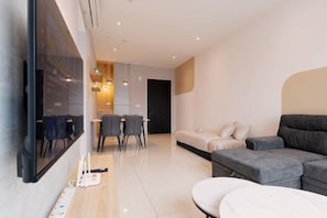 A modern living room with a sofa, a dining table with chairs, a TV mounted on the wall, and a kitchen area in the background. - Datum Jelatek Residence by FEEL HOME (Ampang)